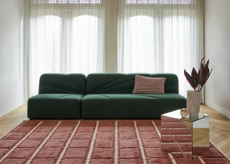 Grünes Hana Sofa von Jesper Home auf einem rot gemusterten Teppich vor hellen Vorhängen