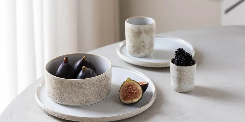 Schale mit Feigen, flache Teller und kleine Becher aus gesprenkeltem Steinzeug von S|P Collection auf einem hellen Tisch